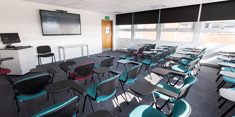 Empty teaching room set up with empty chairs facing front, towards digital screen