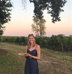 Woman stood outside at sunset, smiling into camera.