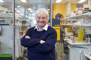 Sir Paul Nurse stood in lab smiling with arms folded in front of him.
